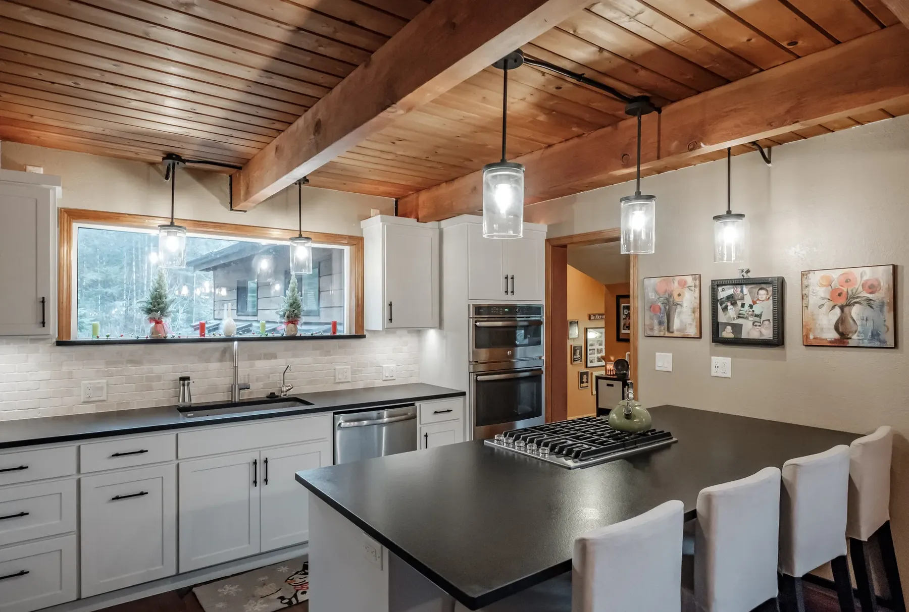 The Corvallis kitchen after: white cabinets, a black island with cooktop and pendant lights under the same wood ceiling