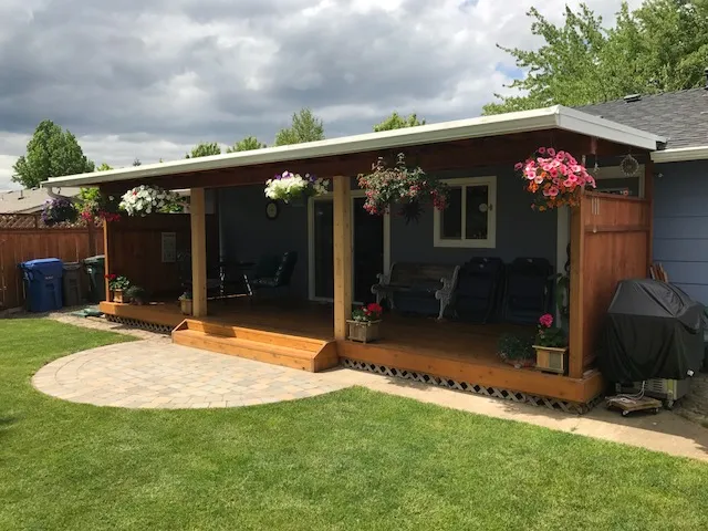 A covered porch with hanging flower baskets and a paver patio