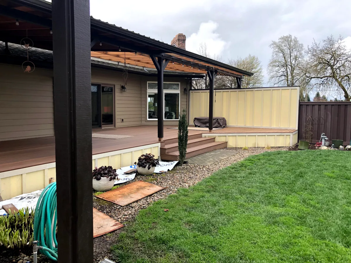 A covered deck with a dark roof and timber posts above the lawn
