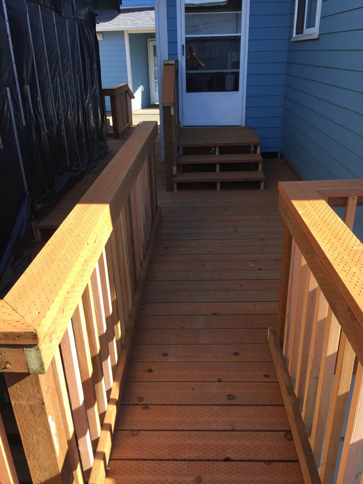 A cedar ramp with railings leading to a blue house