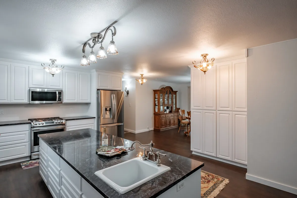 A kitchen island with a sink, white cabinets and track lighting