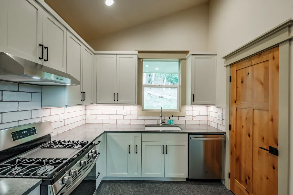 A kitchen with sage cabinets, a white subway backsplash and a knotty alder door