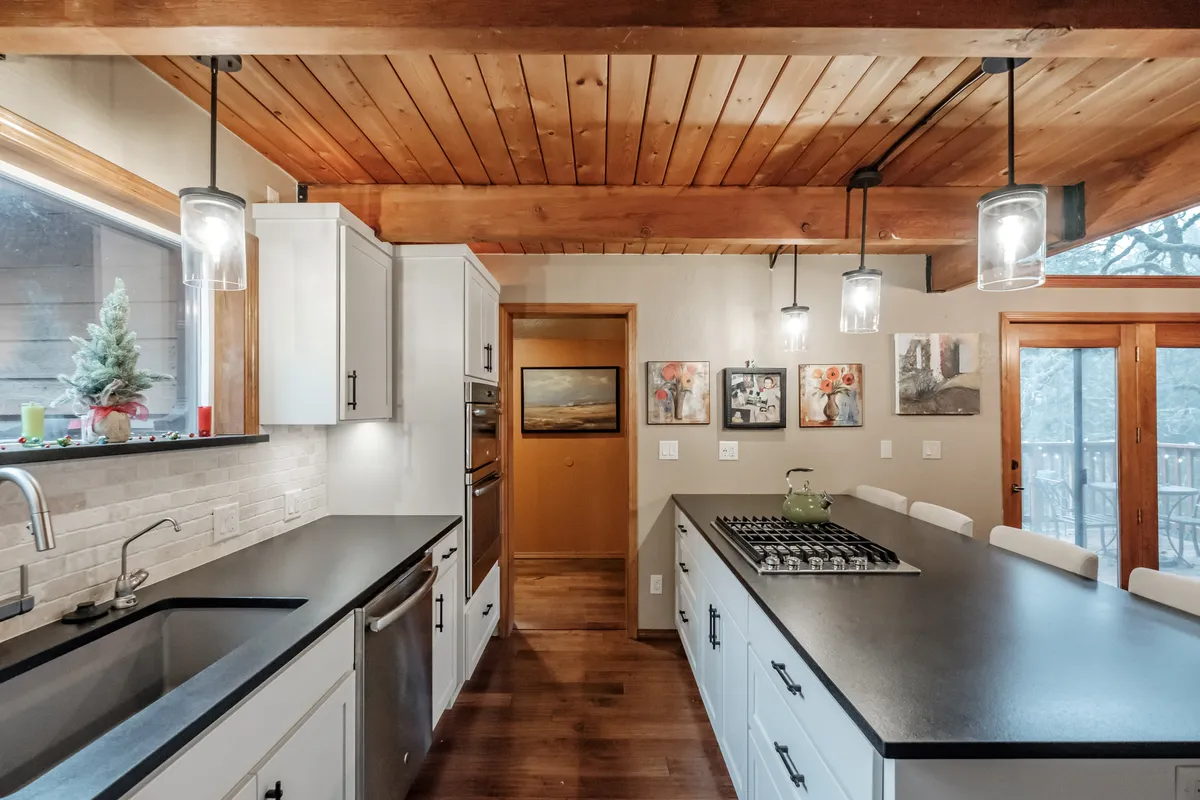 The remodeled Corvallis kitchen with white cabinets and a black island under a wood ceiling