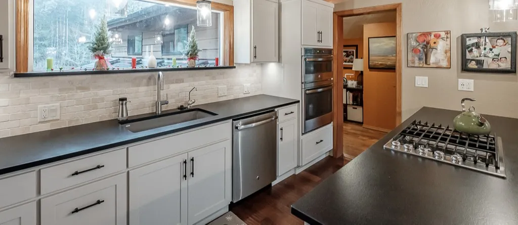 The remodeled Corvallis kitchen with white cabinets and a black island under a wood ceiling