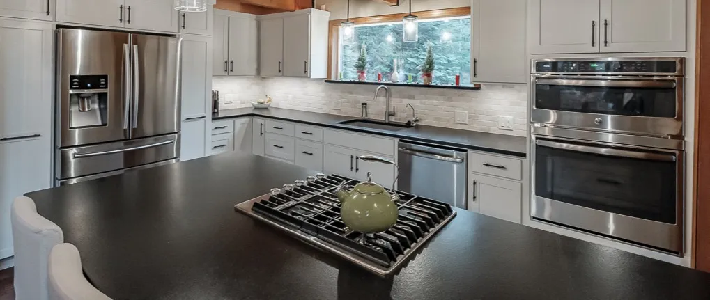 The remodeled Corvallis kitchen with white cabinets and a black island under a wood ceiling