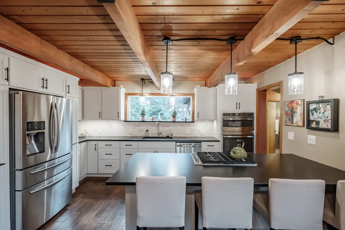 The remodeled Corvallis kitchen with white cabinets and a black island under a wood ceiling