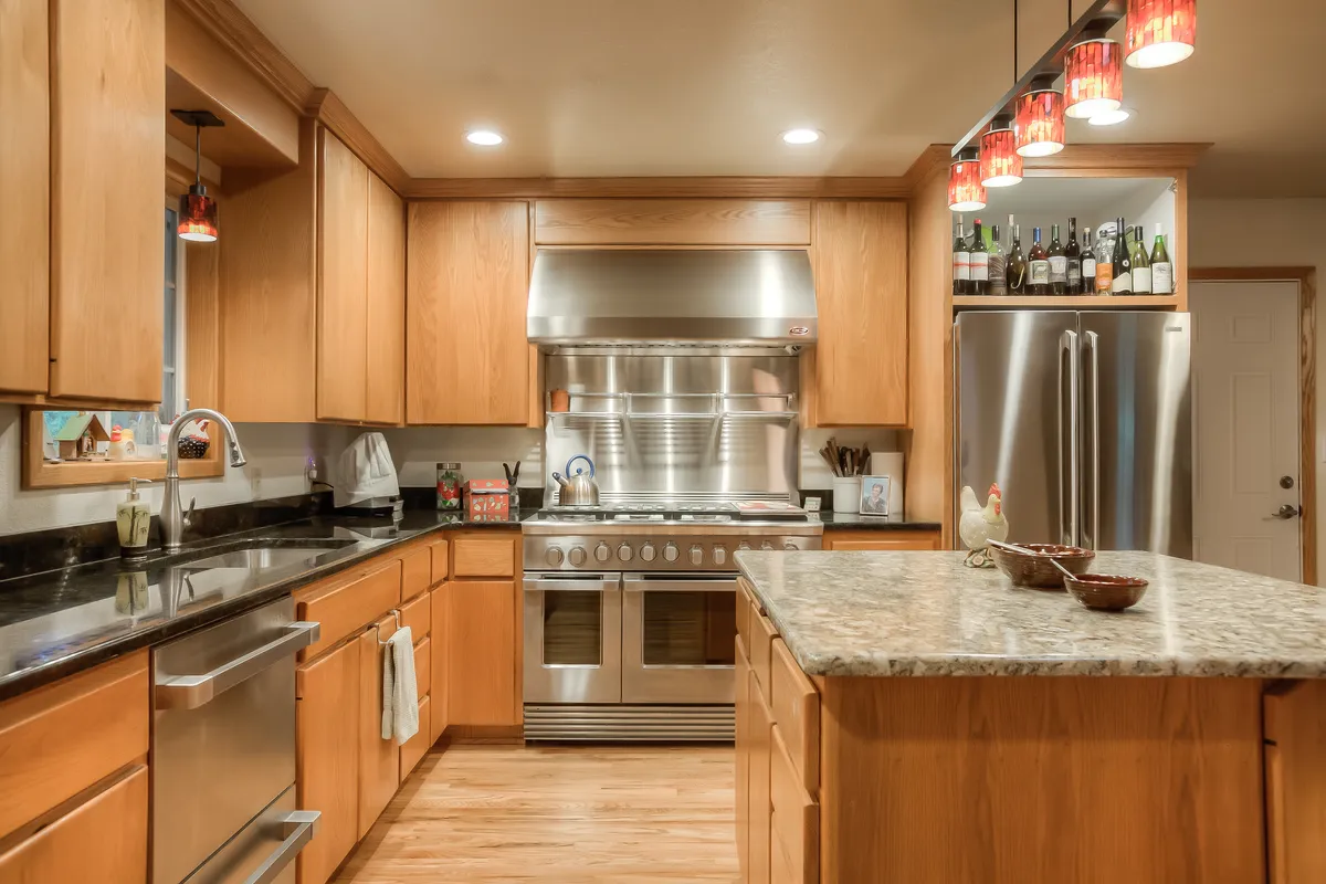 The refreshed kitchen with wood cabinets, granite and a stainless hood