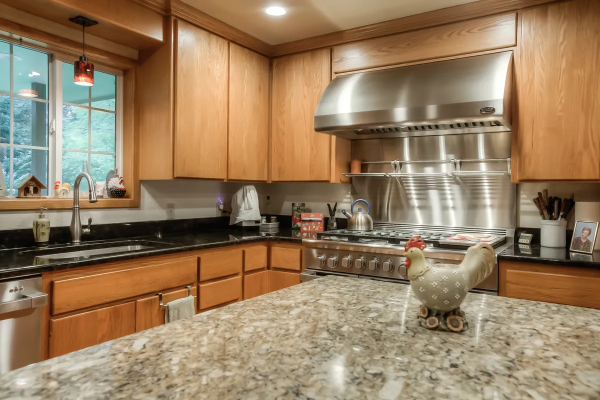The refreshed kitchen with wood cabinets, granite and a stainless hood