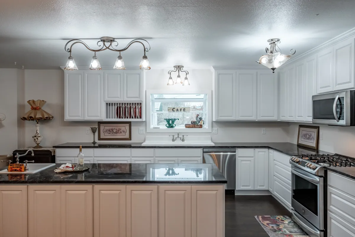 A white kitchen with black granite counters, a peninsula and pendant lights