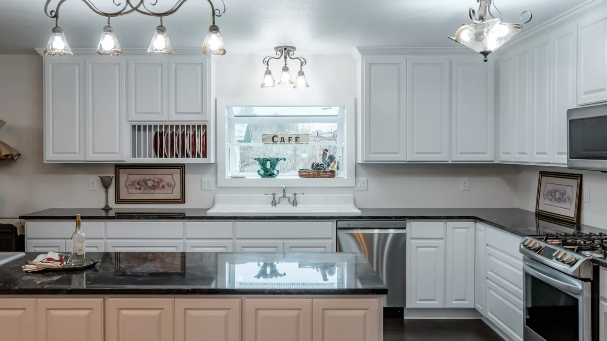 A white kitchen with black counters and a pass-through café window